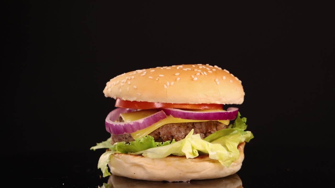 A classic beef burger with lettuce, tomato, onion, and sesame bun rotates smoothly against a black background, under bright studio lighting, highlighting freshness and texture