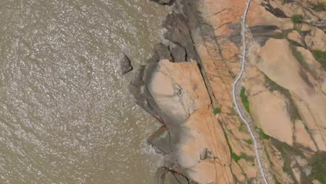 top down slowly rising aerial shot of following the path along a stunning rocky coastline in coloane, macau