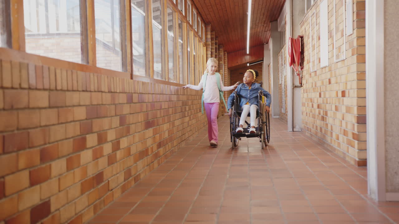 Walking in school hallway, girl pushing friend in wheelchair, smiling together