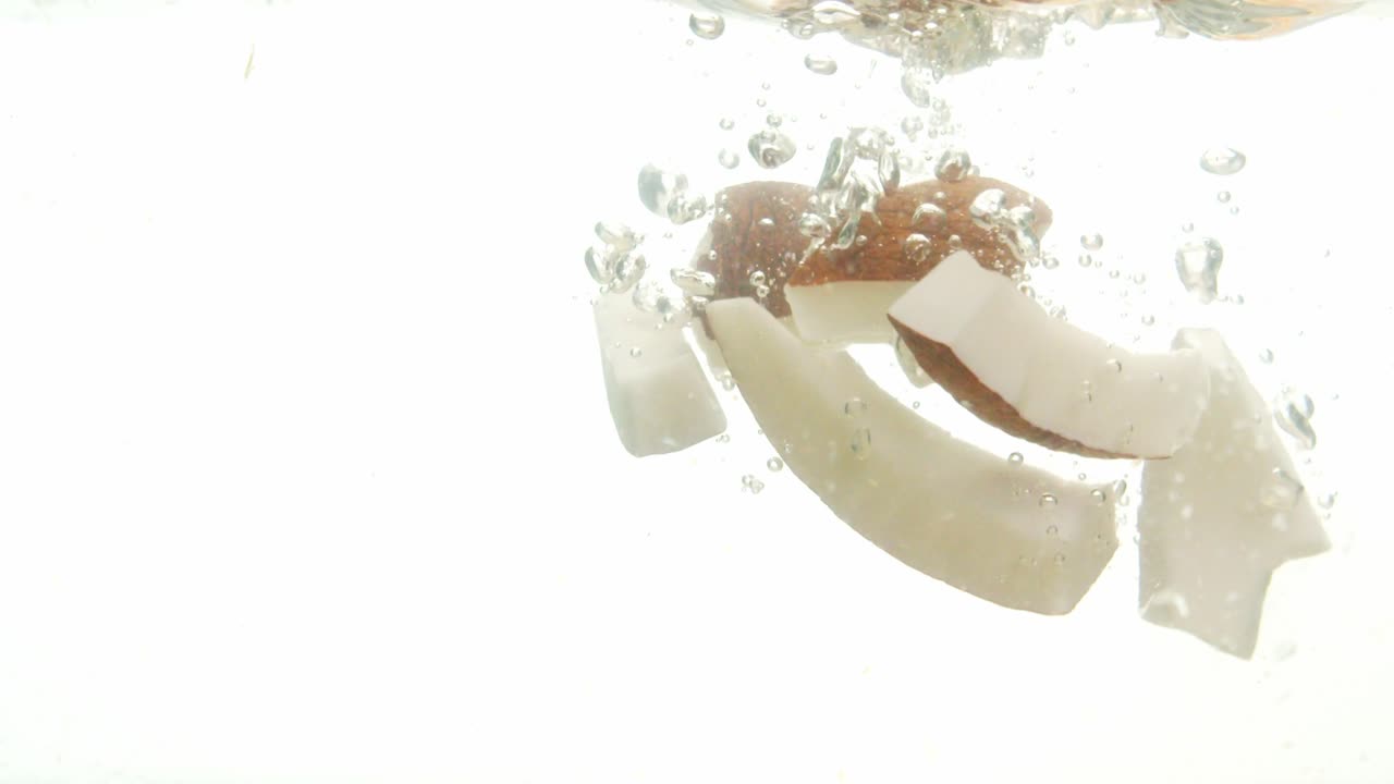 Pieces of fresh coconut dropped into water, isolated on white background