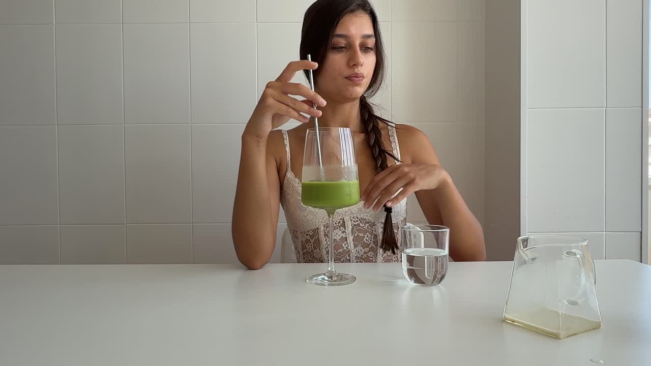 Giovane donna che beve un frullato verde e aggiunge acqua