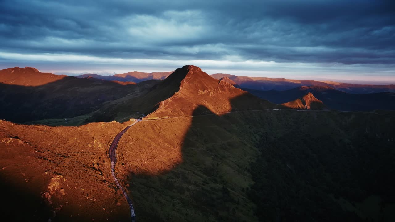 Dramatic drone aerial view of an ancient volcano at sunset, the sky is dark, Auvergne - Puy Mary, France
