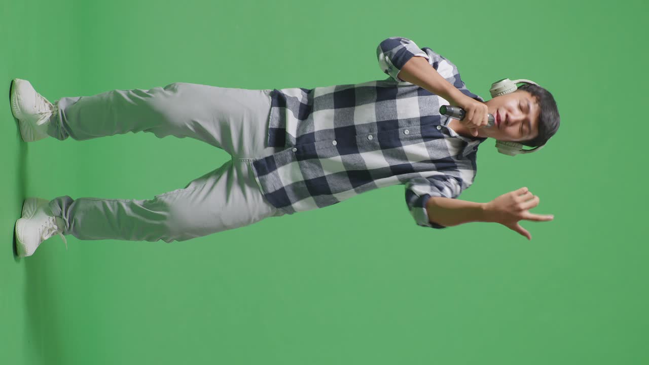 Full Body Of Young Asian Teen Boy Wearing Headphone And Holding A Microphone And Rapping On The The Green Screen Background