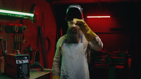 portrait shot of caucasian welder man taking off face shield or protective mask and smiling at camera in workshop