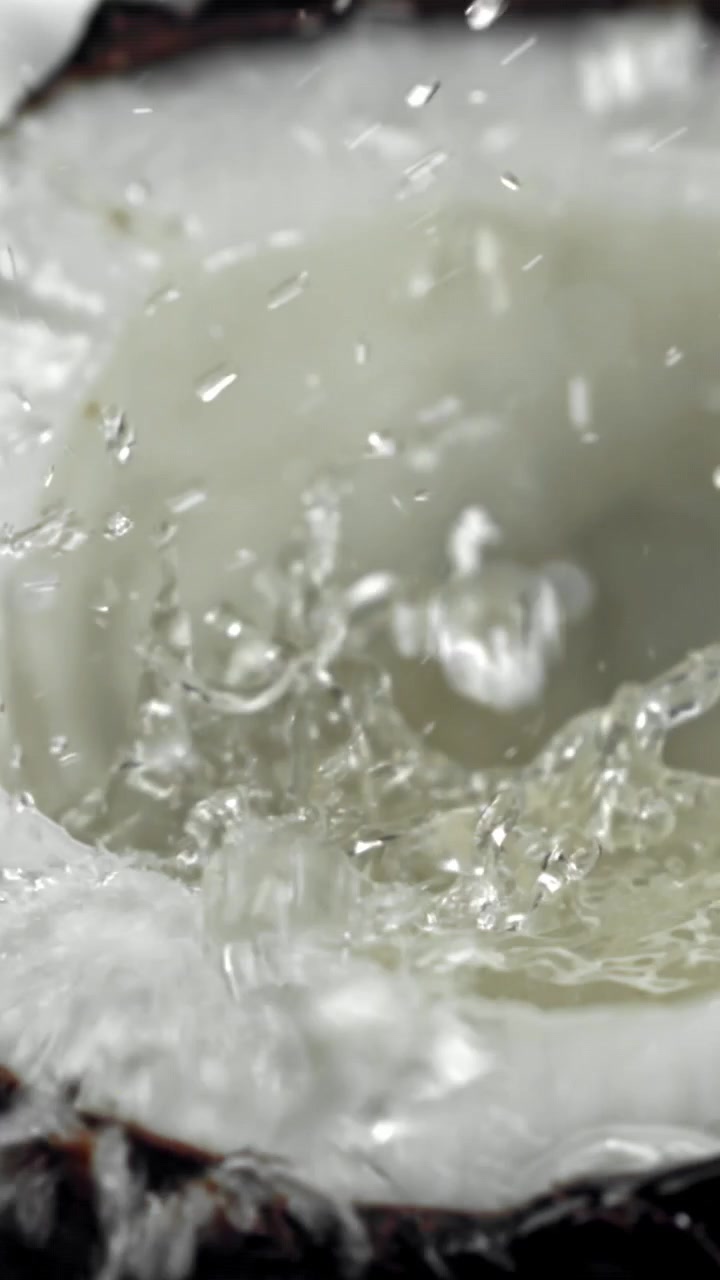 Acqua di cocco rinfrescante che schizza in una noce di cocco tagliata a metà