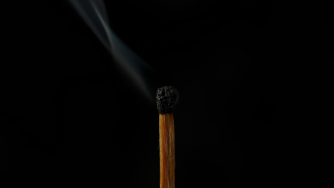 un solo fósforo quemado contra un fondo negro con humo que se eleva