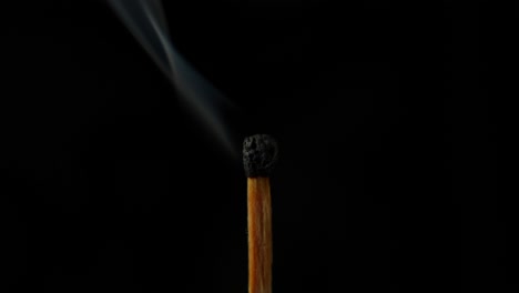 single burned matchstick against a black background with smoke rising