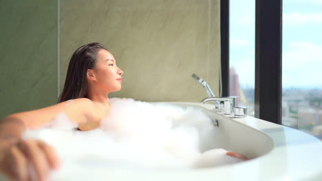 close-up of a beautiful woman in a luxurious bubble bath has a view of a modern city out of the window