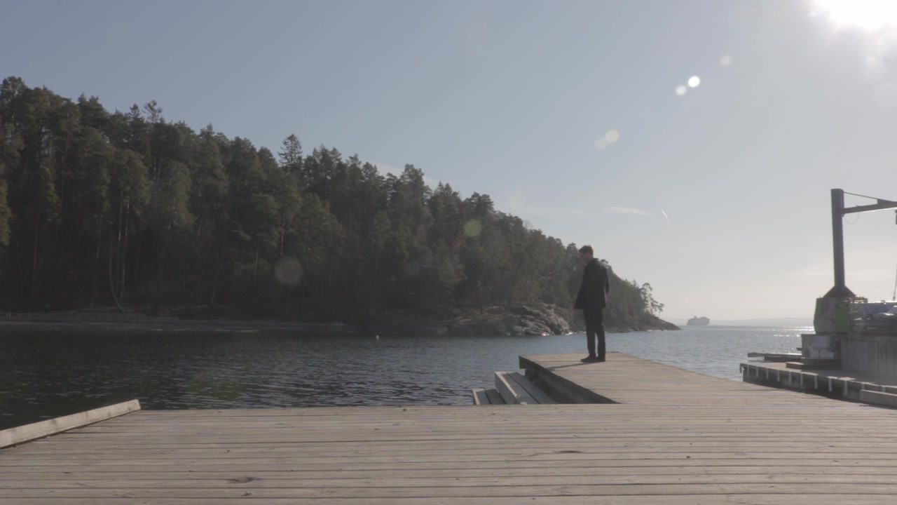 Pria berjalan sendirian di dermaga kayu, memandangi air tenang fjord Oslo di Bygdoy, Norwegia