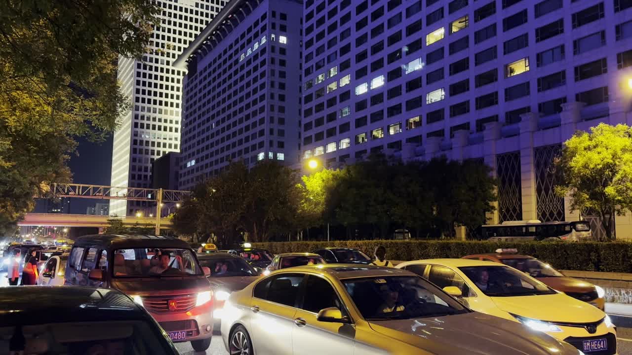 Congestion along the sidewalk in Beijing, with a striking purple-lit building in the distance