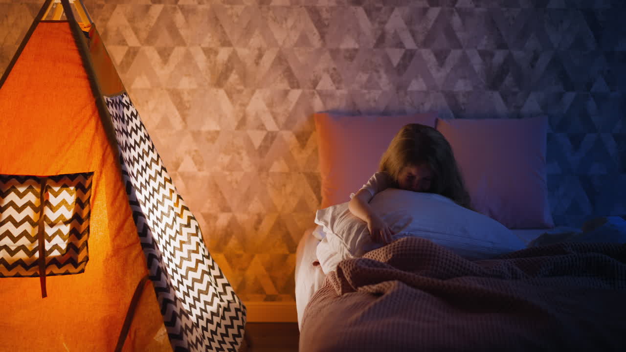 슬픈 작은 아이는 티피와 함께 반 어두운 방에서 침대에 울고