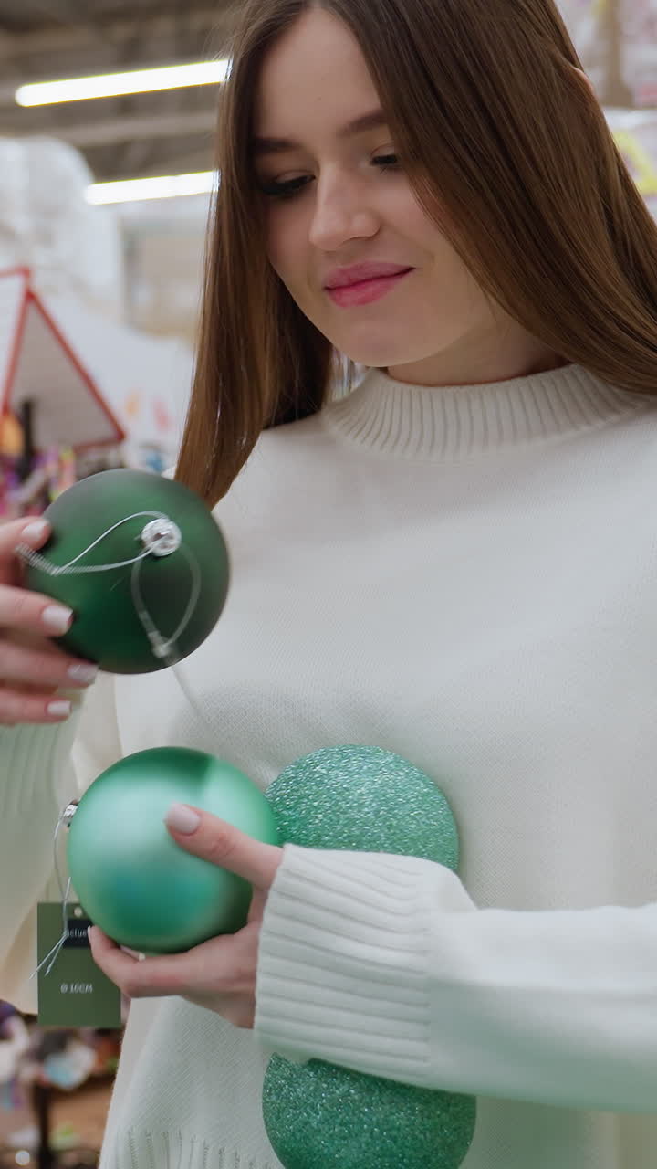 Young woman carrying beautiful green and shimmering ornaments in a decor store, some of them falling to the ground while she admires them