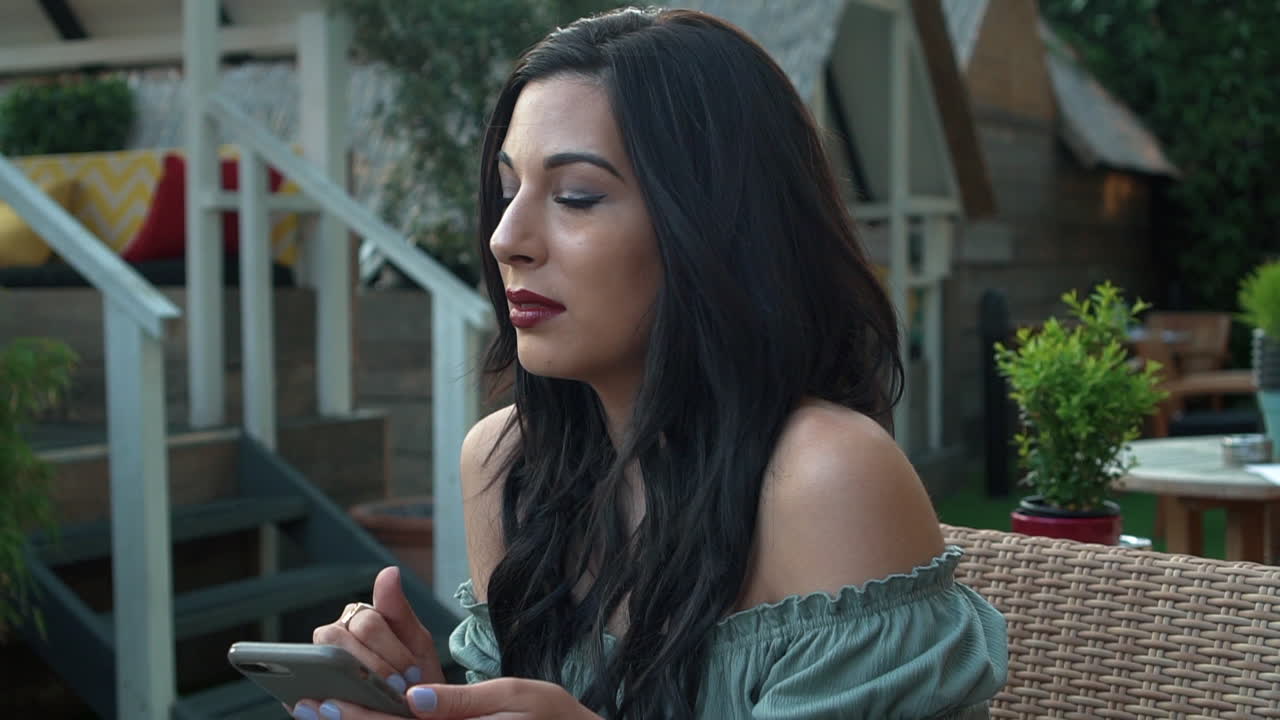 joven morena segura y atractiva con un top informal, usa su teléfono celular, sonríe alegremente a los mensajes de texto, mira a su alrededor