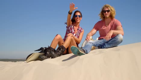 couple with sand board sitting and pointing at a distance in the desert 4k