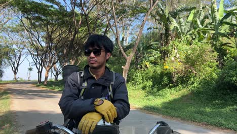 tilt up shot of biker take a rest on motorbike while wearing sunglasses at the countryside road
