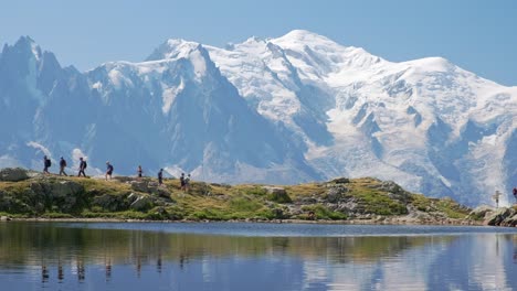 people hiking with reflections of the mountains, and behind the view of the mont blanc, in the valley of chamonix, in france in a sunny day