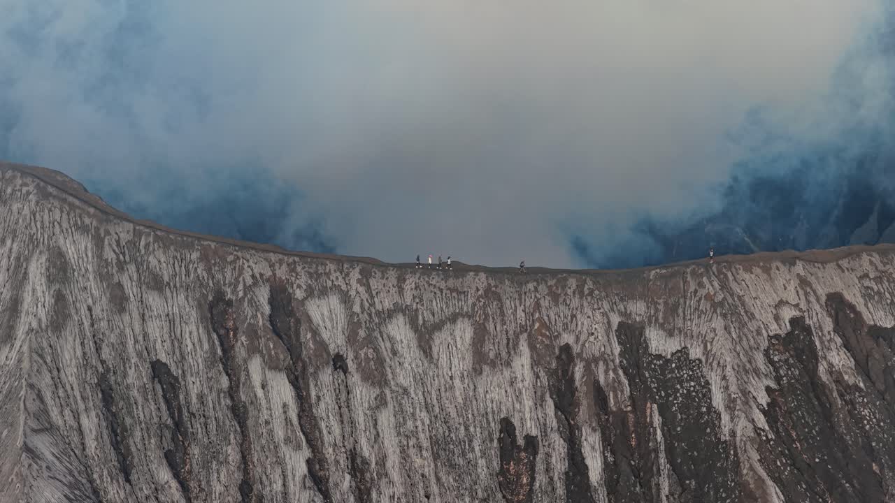 Turisti che camminano sul bordo del cratere del vulcano Bromo fumante.