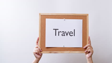 woman's hand shows the paper on board with the word travel in white studio background with copy space