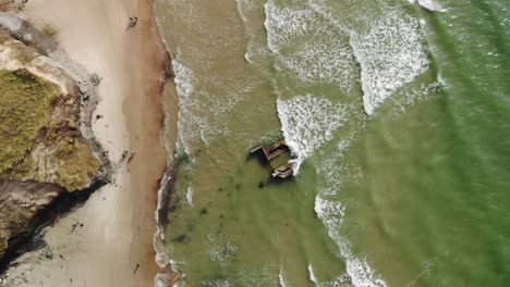 Aerial-top-down-of-waves-crashing-against-old-German-bunker-laying-on-at-the-Danish-west-coast-while-it-is-slowly-eroding