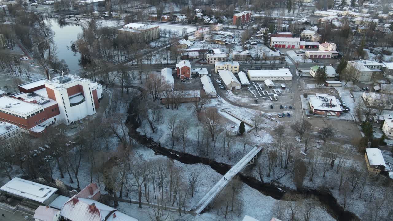 A breathtaking aerial view of Valmiera city, showcasing the winding Gauja River surrounded by snow-covered landscapes and residential areas under a wintry sky.