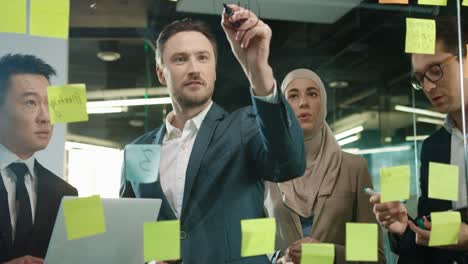 Close-Up-View-Of-Multiethnic-Business-People-Group-Working-In-A-Modern-Office-While-Writing-On-Glass-In-A-Cabinet-With-Sticky-Notes-3