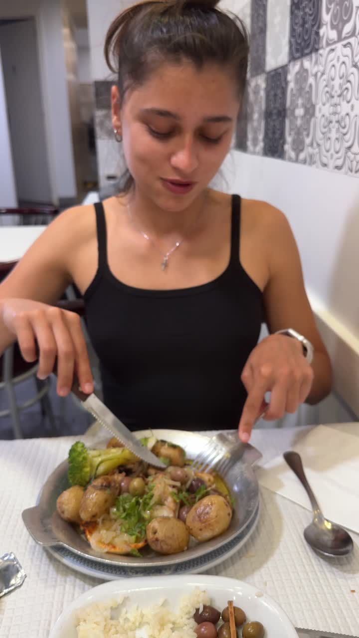 Woman eating a meal with potatoes, broccoli, and olives at a restaurant