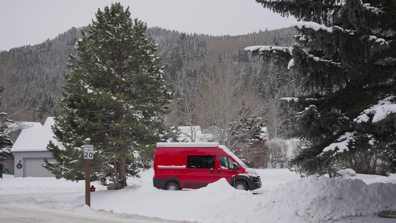 Furgone rosso parcheggiato in un villaggio e paesaggio montano innevato in una fredda giornata invernale.