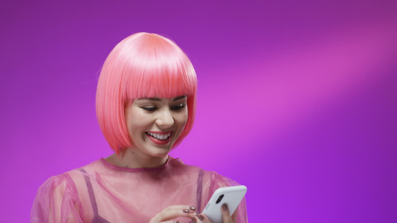 primer plano de una mujer bonita con una elegante peluca rosa sonriendo alegremente con un teléfono inteligente en las manos 1