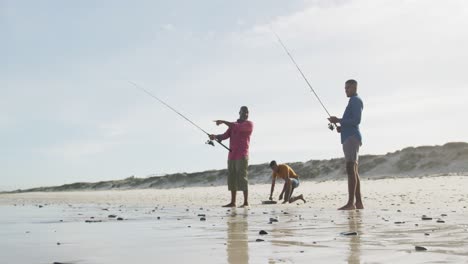 african american senior father and two teenage sons standing on a beach fishing and talking