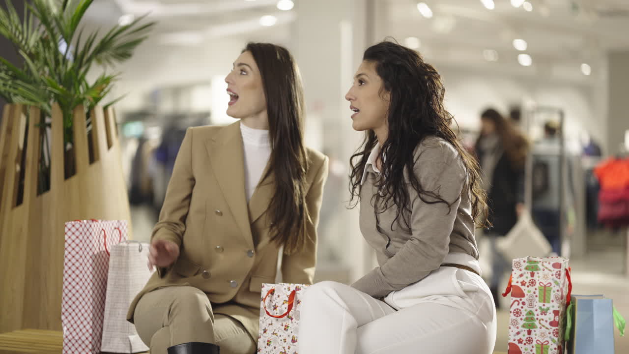 Two women sitting with shopping bags in a modern mall