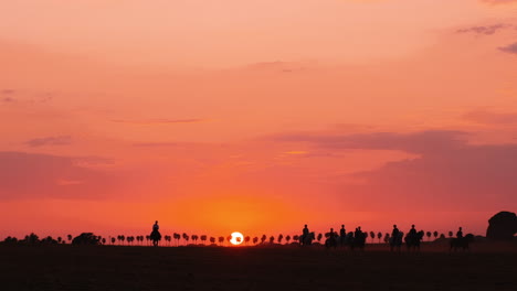 silhouette of several people riding horses during beautiful orange colored sunset in background