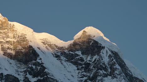 snowy mountain ridge with blue sky in nepal, snowcapped mountains scenery in snow with steep mountain face in first light at dawn with light on top of mountain in himalayas mountains at annapurna