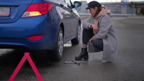 mujer cambiando un neumático al costado de la carretera