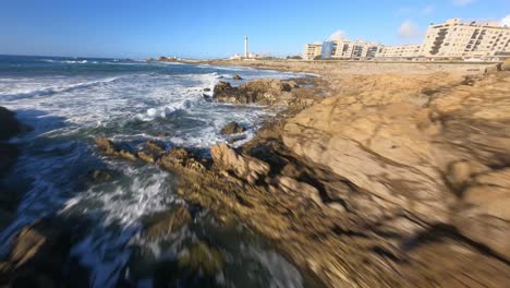 Epic-drone-FPV-low-over-ocean-waves-and-rocks-to-passing-lighthouse-on-coastline