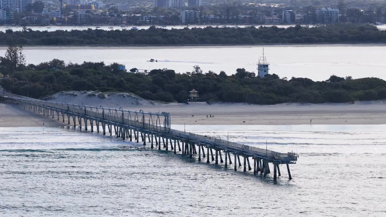 Ampia inquadratura dall'alto del pontile industriale per il bypass della sabbia che si estende nelle onde dell'oceano.
