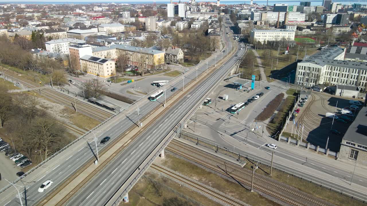 Aerial drone footage flying forward over Tallinn Pärnu highway bridge that is going over railroad or traintracks during a sunny day in Tallinn central city. Cars, vehicles and trams are seen driving.