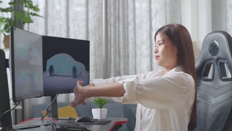 side view of asian female automotive designer stretching while working on 3d model of ev car on the desktop computers in the studio