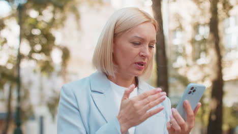 caucasian mature businesswoman looking shocked while reading bad news on mobile phone on city street
