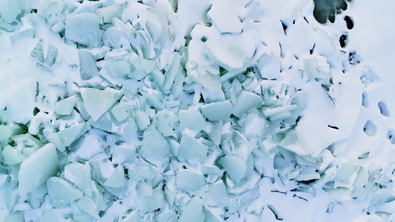 Vista dall'alto da drone di ghiaccio marino fratturato e di una pozza di acqua di disgelo verde limacciosa, con lastre di ghiaccio bianche spezzate e strutture ghiacciate che formano un motivo invernale astratto