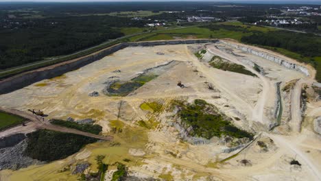 aerial drone video flying above a large limestone quarry mine where puddles of yellow residue water and gravel piles and mountains are visible with heavy equipment during a sunny day in countryside
