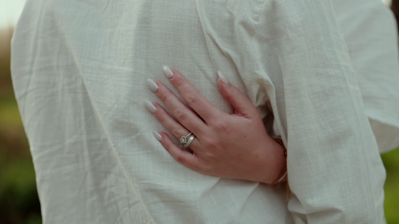 Closeup of woman hand with ring resting on partner shoulder wearing light clothing showing affection and relationship detail