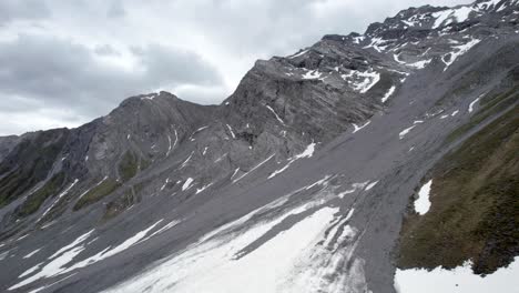 Aerial-drone-footage-rising-slowly-amongst-dramatic,-jagged-mountain-slopes,-looing-towards-snow-covered-ridges