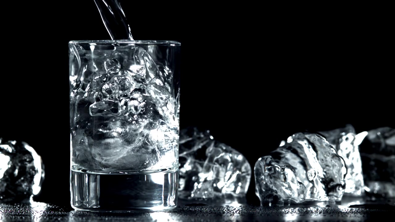 Versamento di acqua al rallentatore in un bicchiere con cubetti di ghiaccio