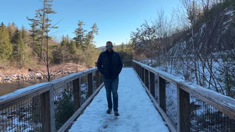 Mann,-Der-Im-Winter-über-Eine-Schneebedeckte-Brücke-über-Einen-Fluss-Geht---Zeitlupe