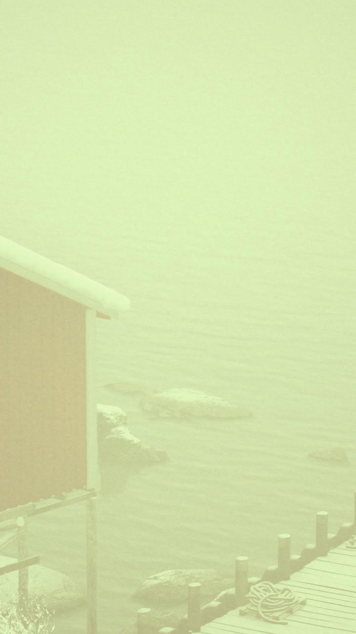 Fog envelops a red cabin and dock on a winter morning by a lake