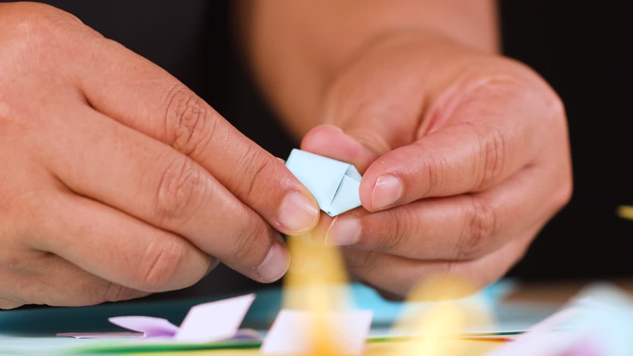 Close up shot of hands using yellow scissors to cut and fold blue origami paper