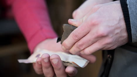 two guys cutting up a brick of hash into smaller pieces on top of a bill