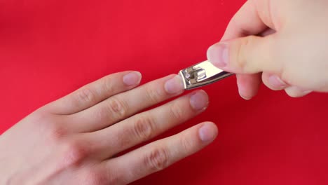 looking down at a person clipping their nails with a metal nail clipper on a red background