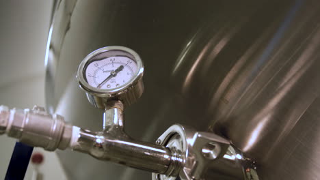 rack focus from a close-up of a pressure gauge mounted on a stainless steel fermentation tank in a brewery to a blurry view