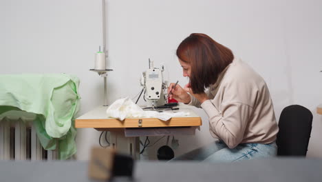 dress maker performs machine maintenance by clipping stuck thread with precise care, ensuring smooth sewing in organized workspace, highlighting calm posture throughout the process